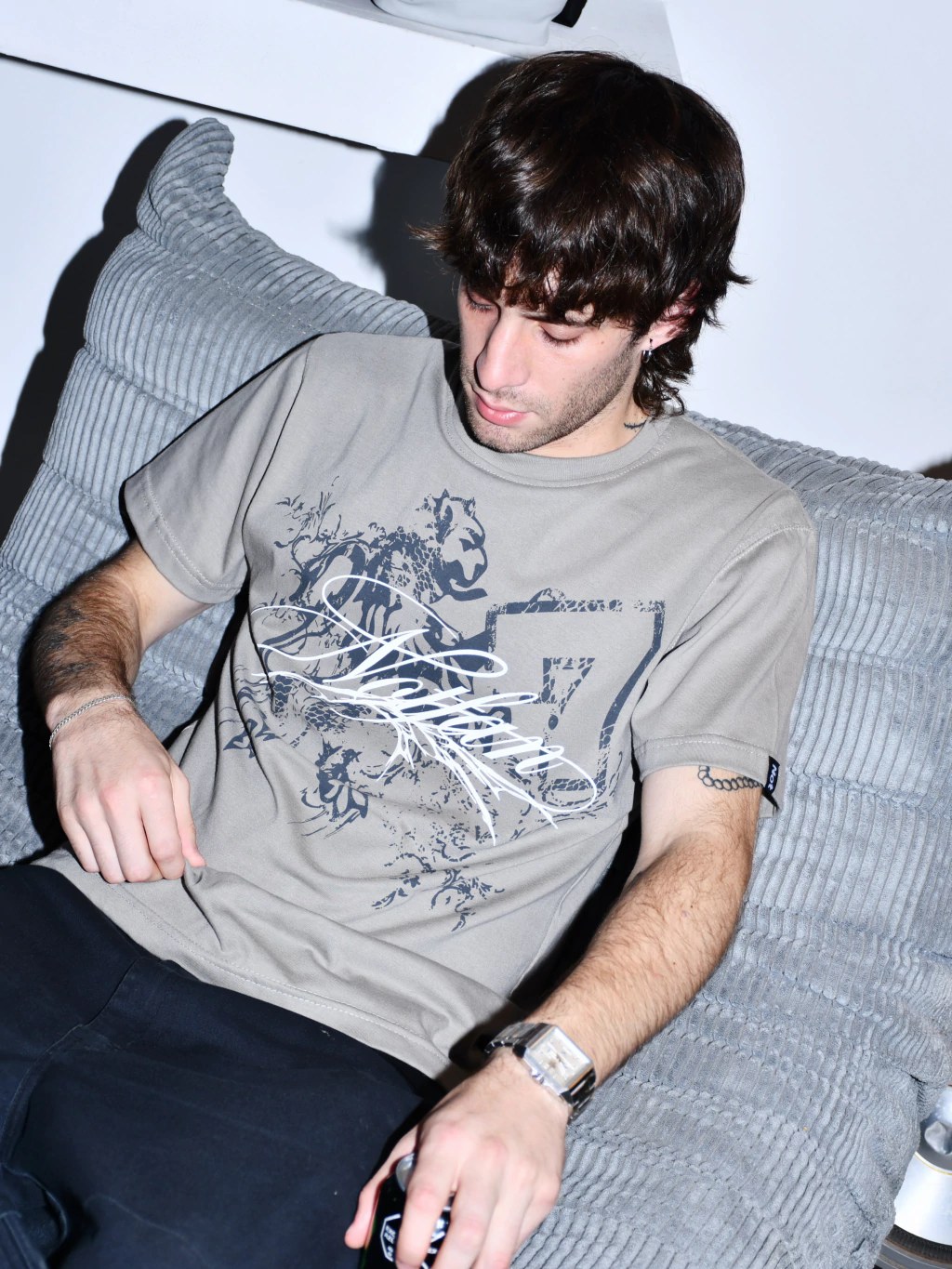 Modelo sentado en un sillón gris con la remera taupe estampada
