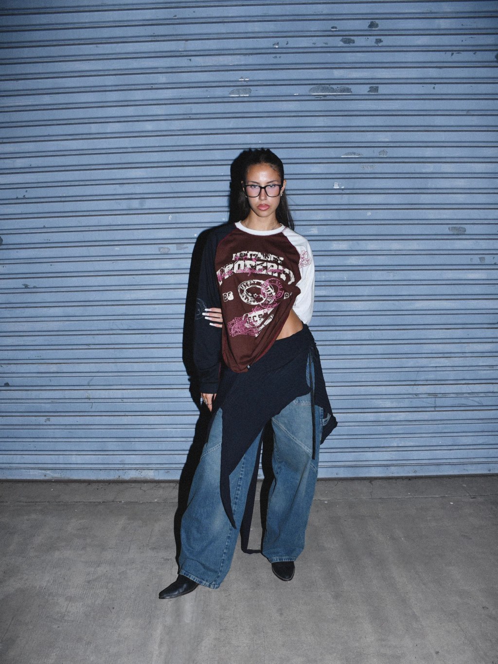 Modelo de pie frente a una persiana azul con la remera marrón